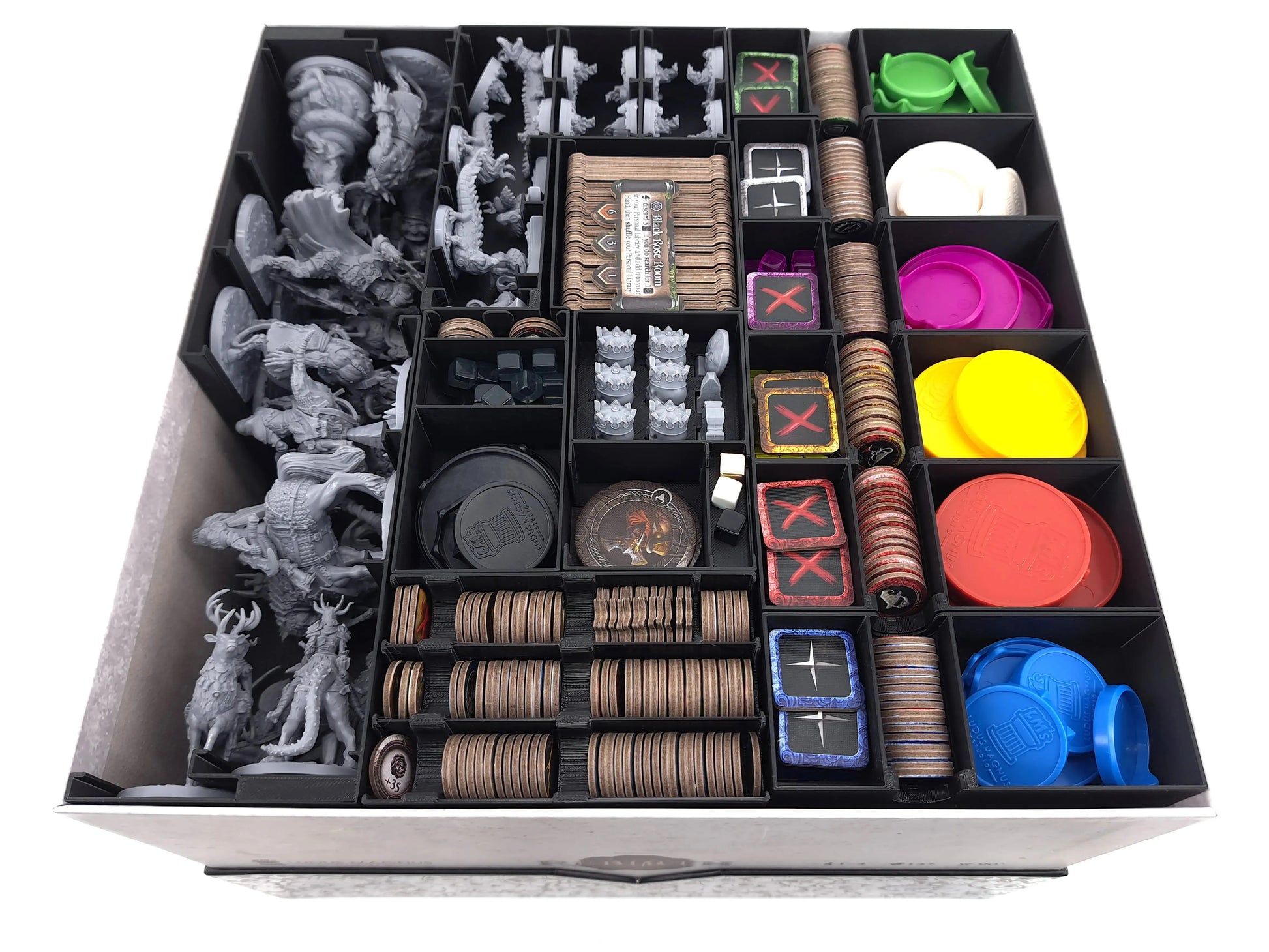 Top-down view of a board game box organized with black 3D printed inserts, holding miniatures, cards, coins, and colored tokens. Modular board game organizer by Tinkering Paws