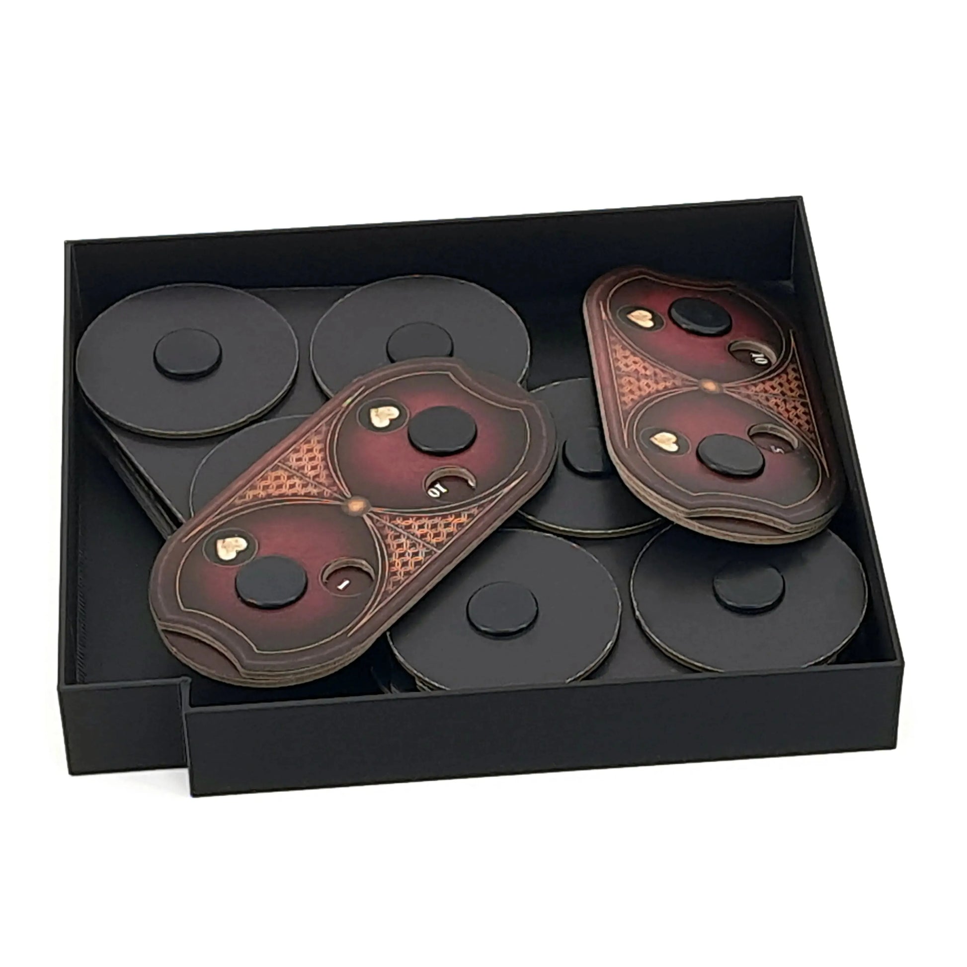 Token storage insert for the Elden Ring board game shown as digital STL files by Tinkering Paws. The image shows a black rectangular 3D-printed tray holding multiple round cardboard tokens stacked flat, along with two elongated, shield-shaped cardboard tokens placed on top. Each token stack is kept organized and separated for quick access during gameplay. This 3D printable board game insert is designed to fit inside the Elden Ring board game box and improve setup, organization, and storage. Digital STL file