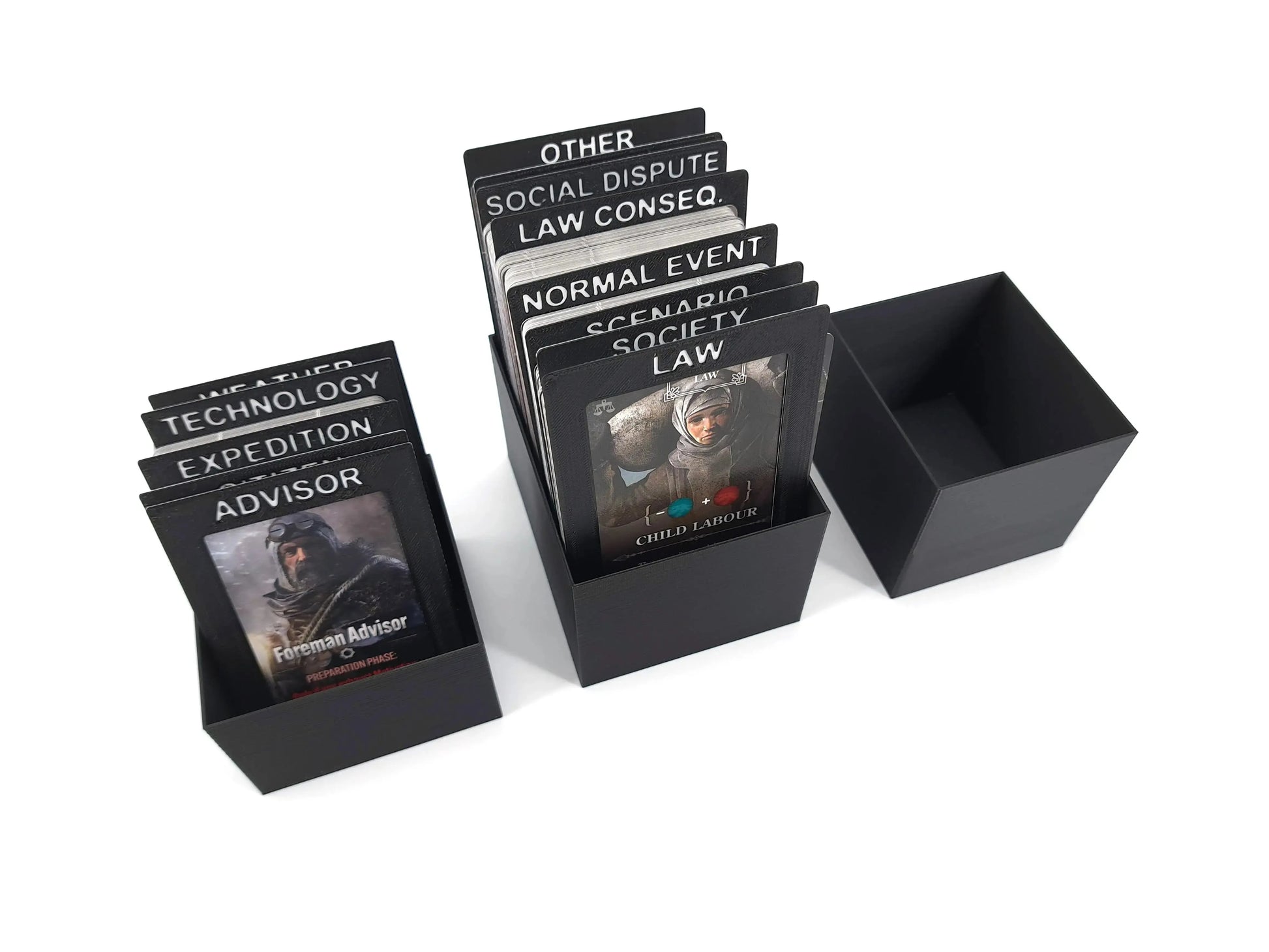 Three black 3D-printed card storage boxes for Frostpunk: The Board Game. Two boxes contain large vertical cards with white labeled dividers such as "ADVISOR," "EXPEDITION," "LAW," and "SOCIETY." One box is empty.